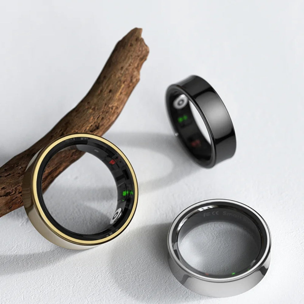 Three smart rings in gold, black, and silver on a light gray background with a wooden branch.