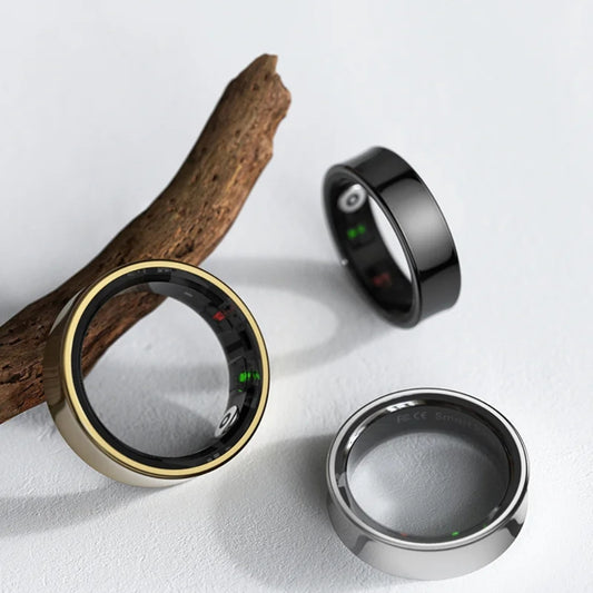 Three smart rings in gold, black, and silver on a light gray background with a wooden branch.